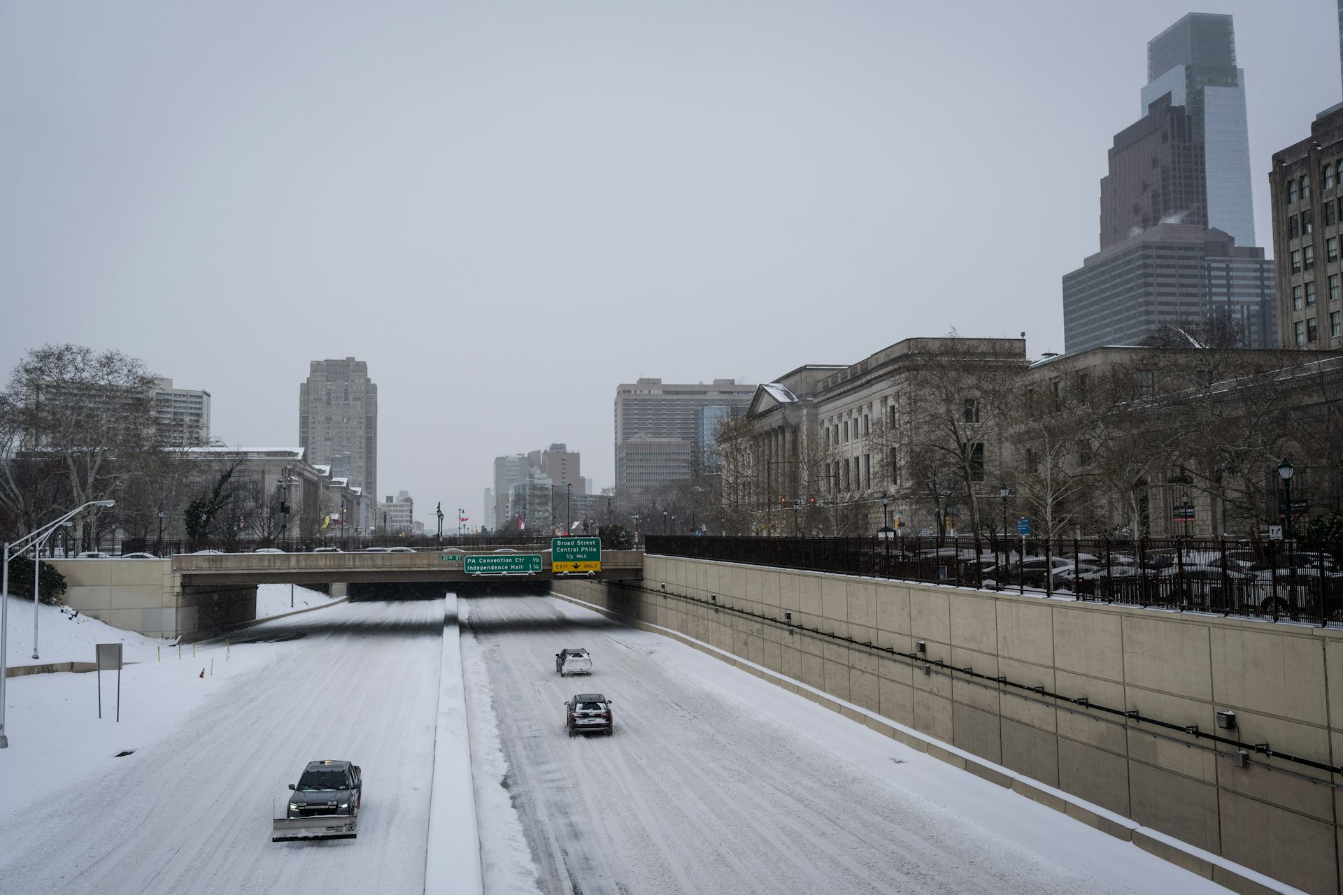 View from overpass of snow-covered highway with two cars and snowplow