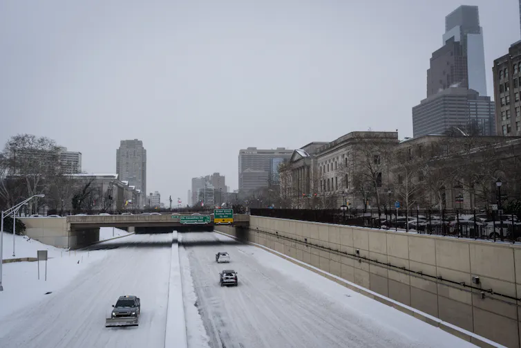 View from overpass of snow-covered highway with two cars and snowplow