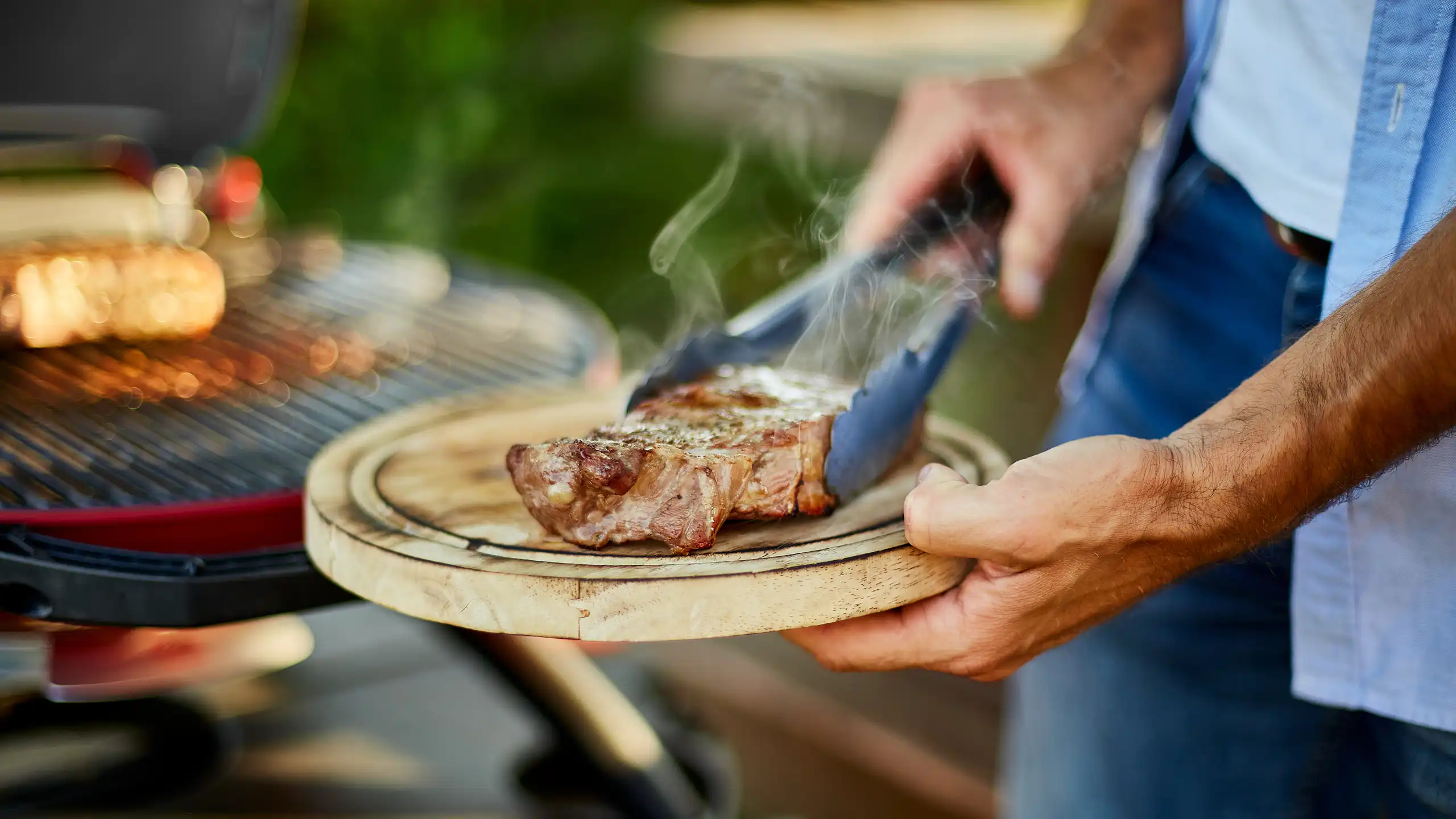 Un homme tient une planche à découper sur laquelle est posé un steak cuit au barbecue.