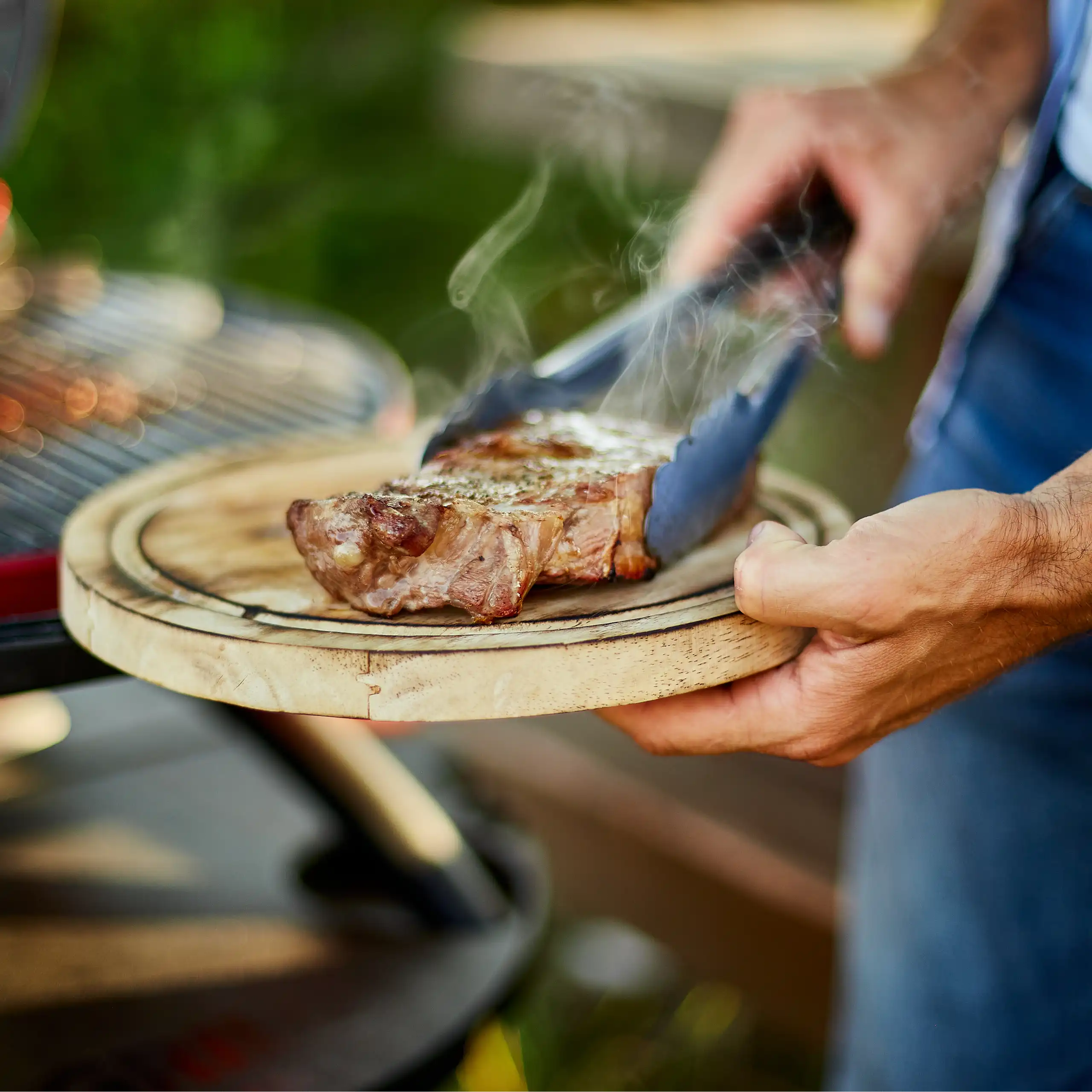 Un homme tient une planche à découper sur laquelle est posé un steak cuit au barbecue.