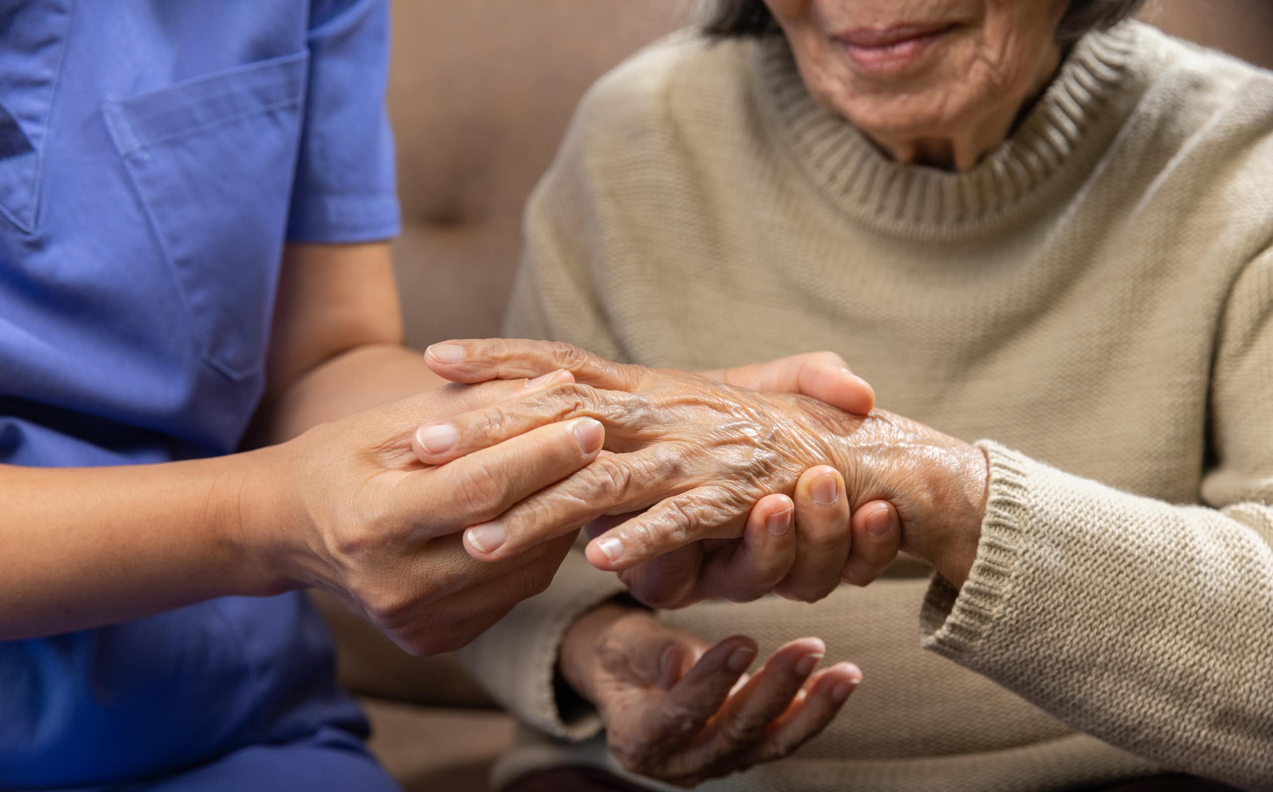 Une aide-soignante en blouse masse les doigts d'une femme âgée.
