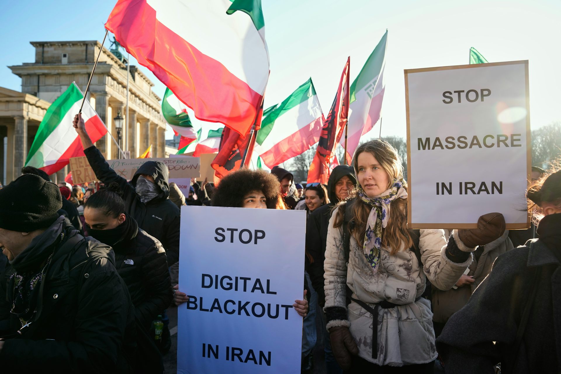A group of protesters carrying signage and waving Iranian flags.