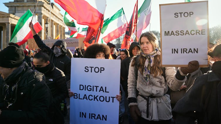 A group of protesters carrying signage and waving Iranian flags.