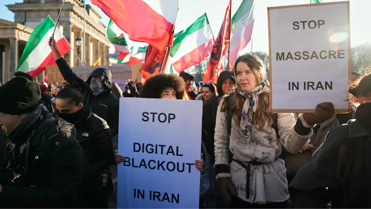 A group of protesters carrying signage and waving Iranian flags.