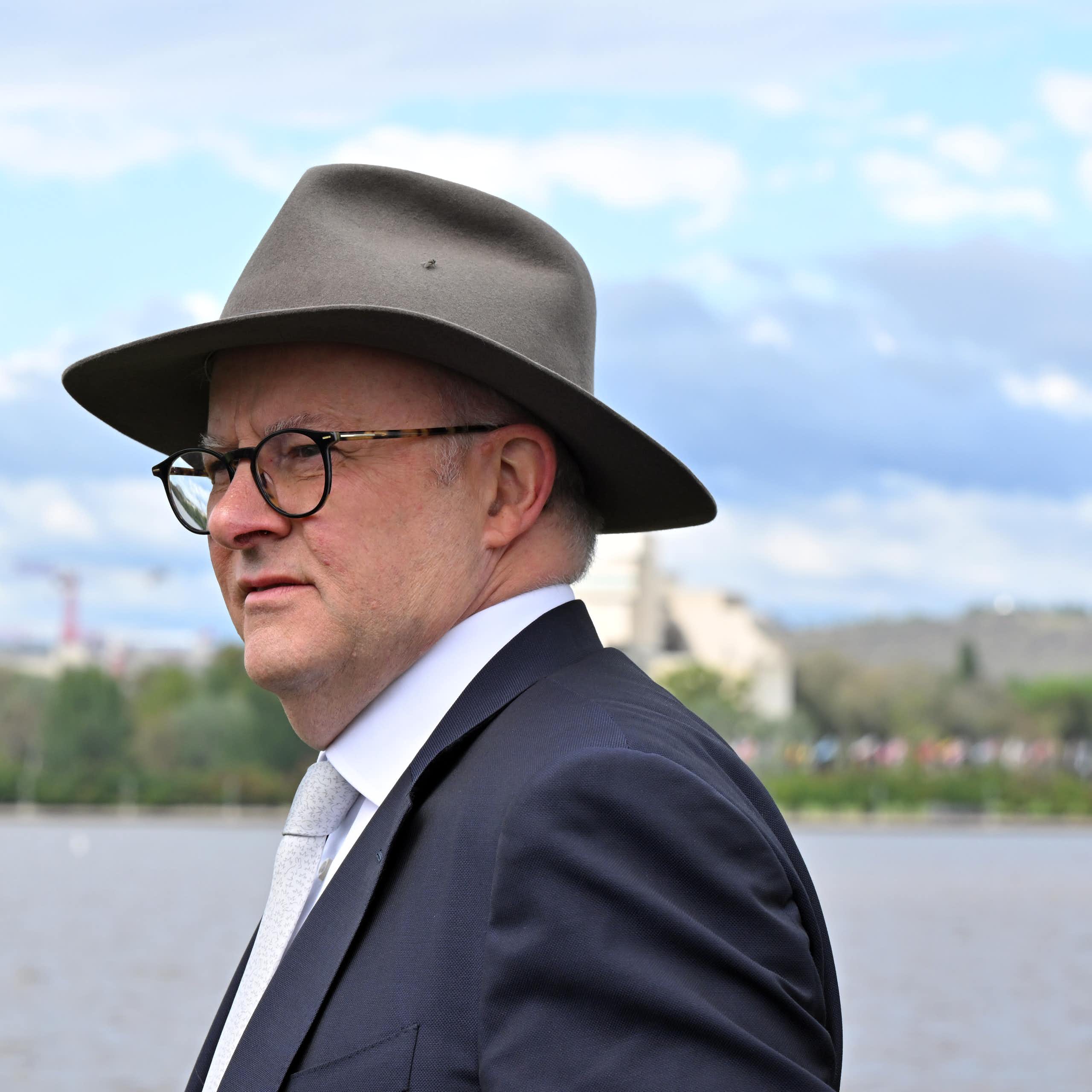 Prime Minister Anthony Albanese, in an akubra hat and suit, looking thoughtful in front of water