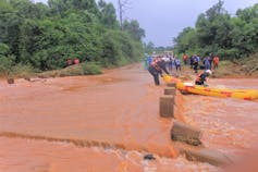 A bridge submerged in orange, muddy flood water with rescue divers entering on a rubber ducky boat