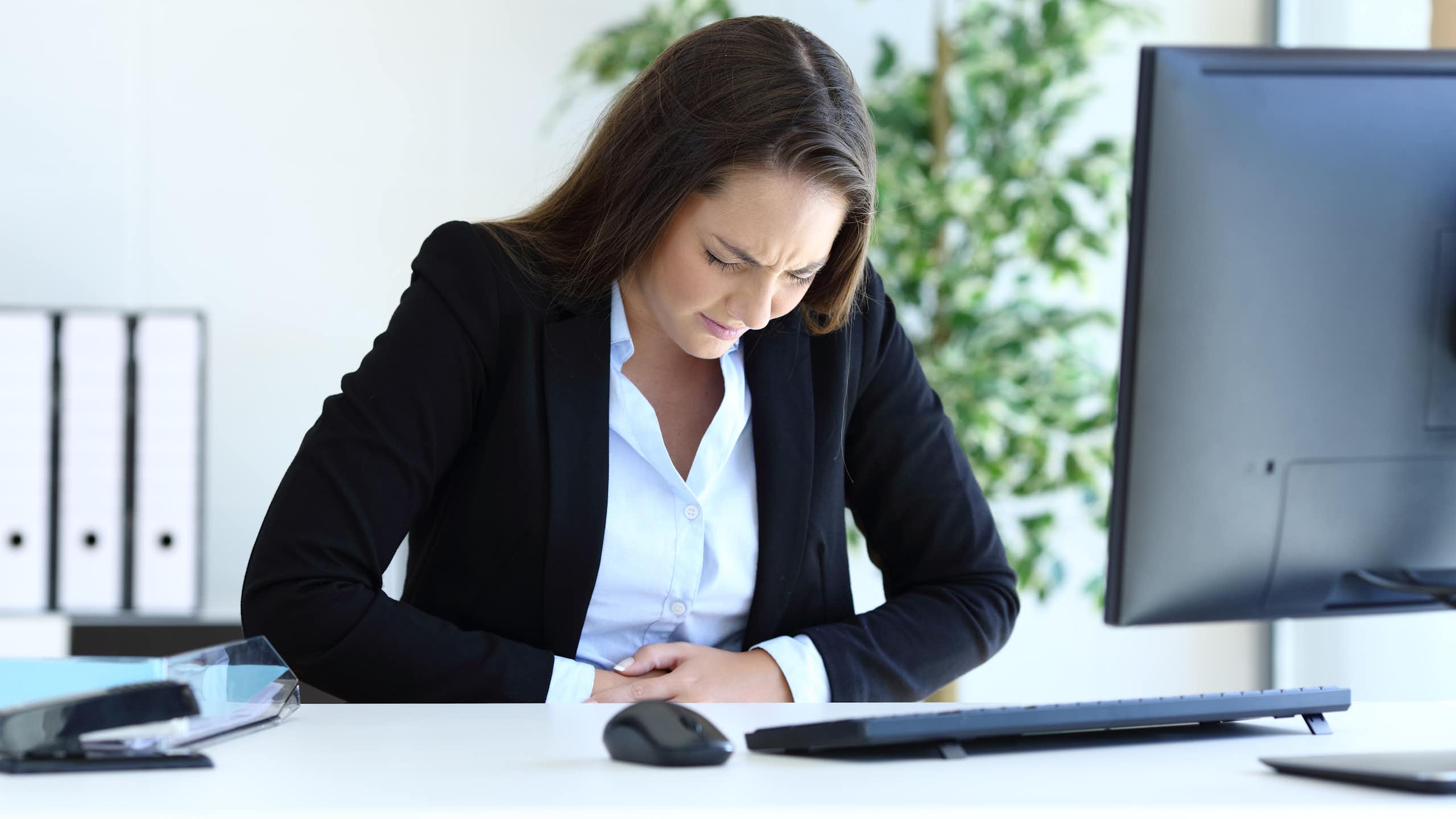 Young businesswoman suffering bellyache working sitting at office