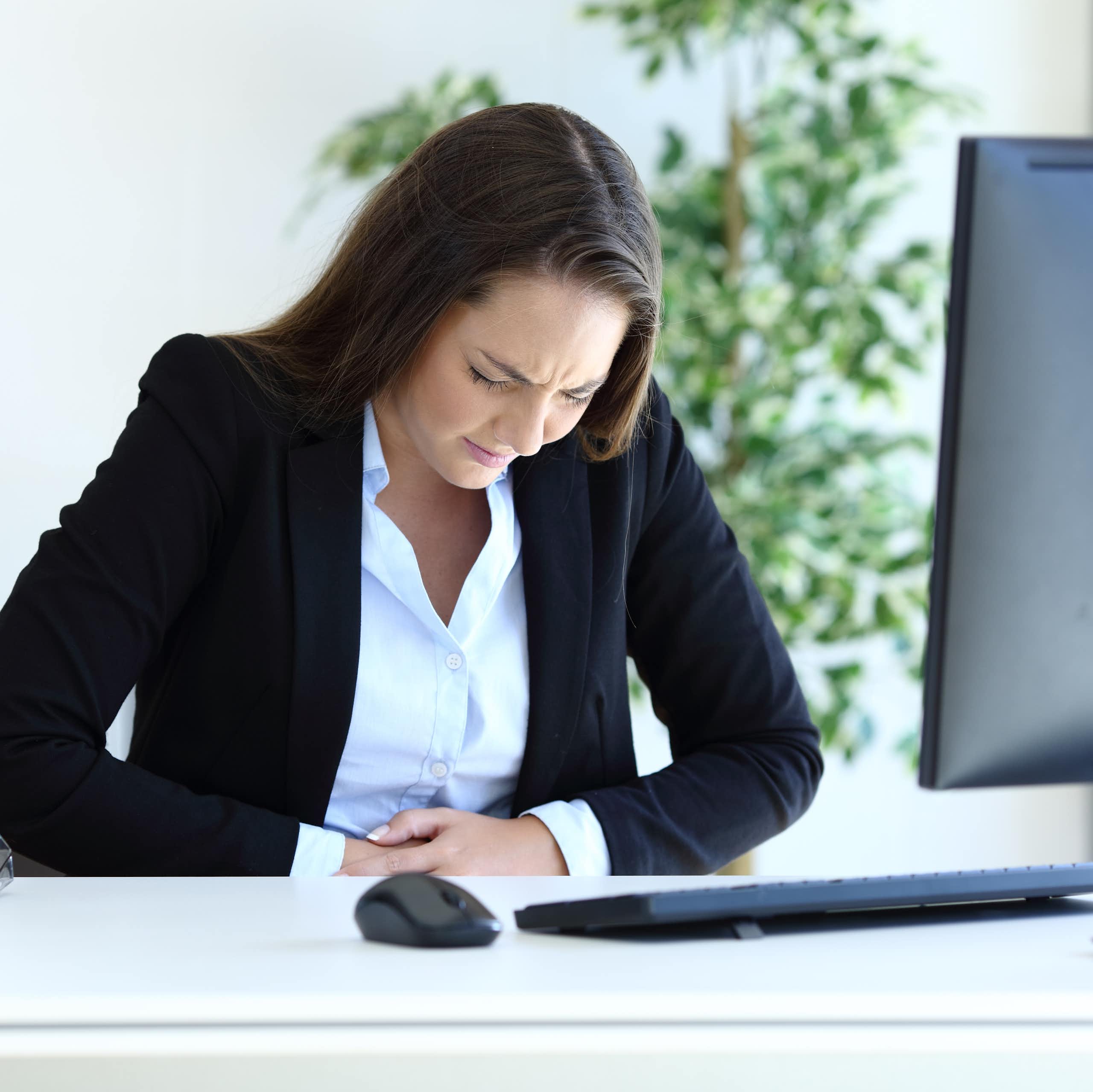 Young businesswoman suffering bellyache working sitting at office