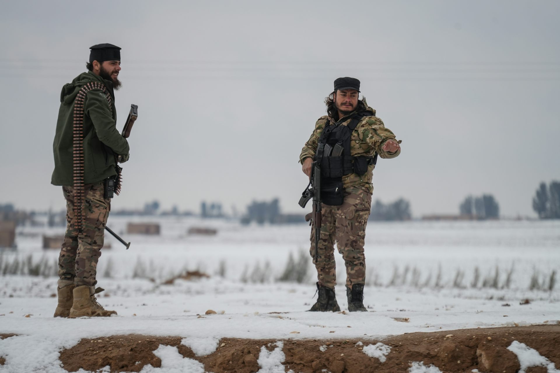 Syrian army personnel stand guard in a snowy field.