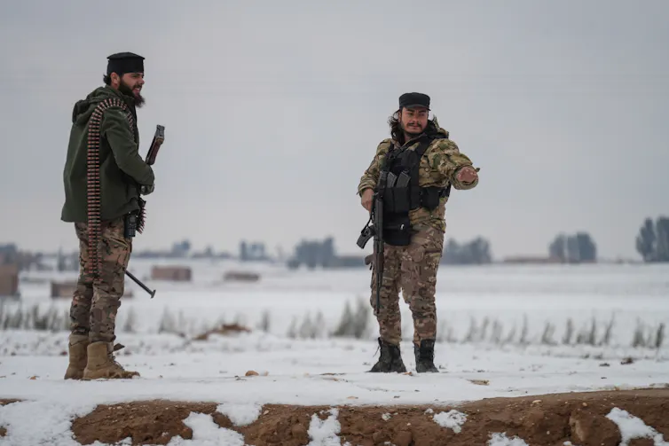 Syrian army personnel stand guard in a snowy field.