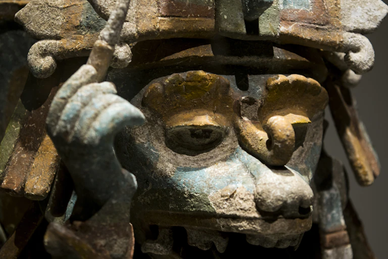 Escultura de un animal con un tocado y sosteniendo un últil de escritura.