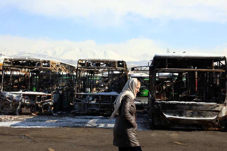 A woman walks past a burnt out bus depot damaged during protests in Tehran.
