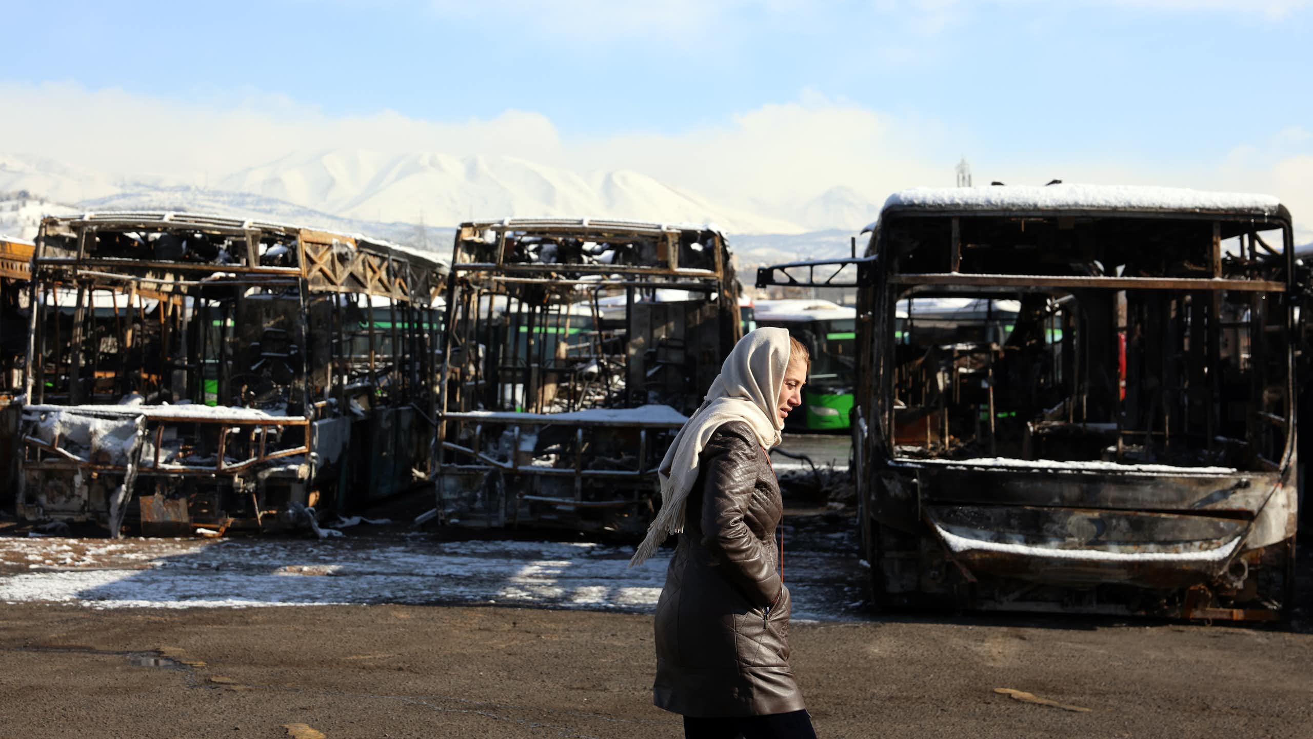 A woman walks past a burnt out bus depot damaged during protests in Tehran.