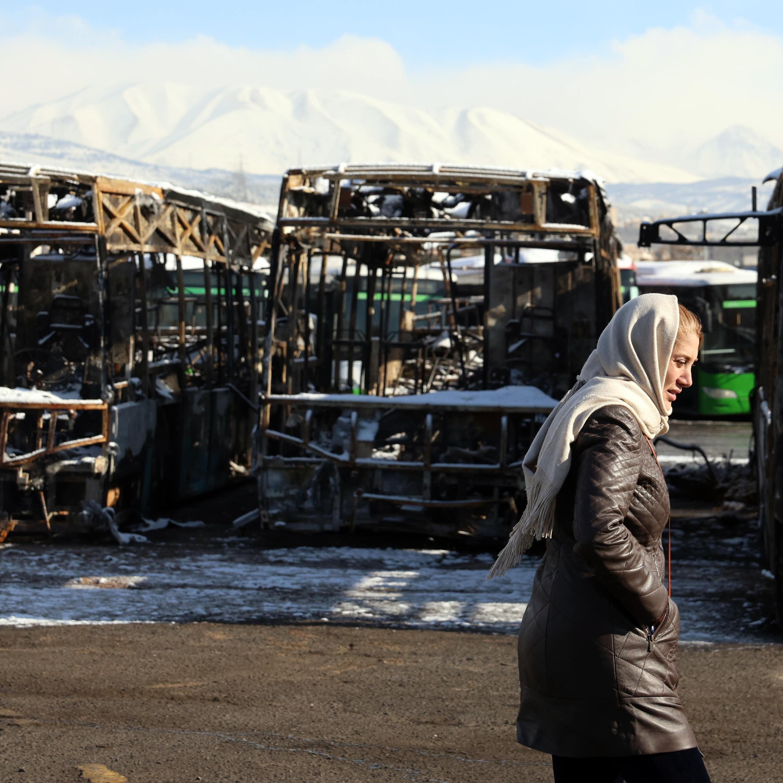 A woman walks past a burnt out bus depot damaged during protests in Tehran.