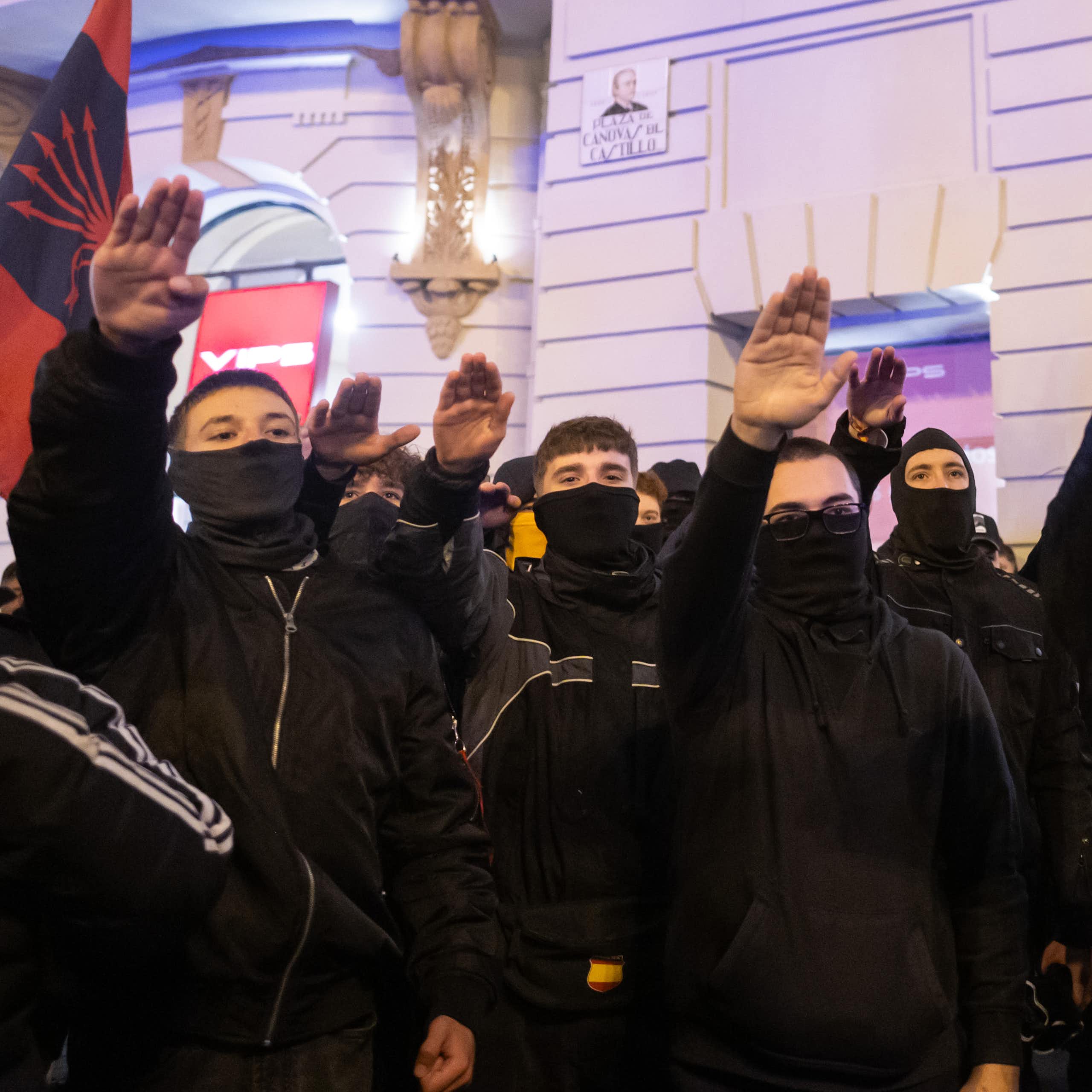 Protesters covered in black make a fascist salute at a protest in Madrid.