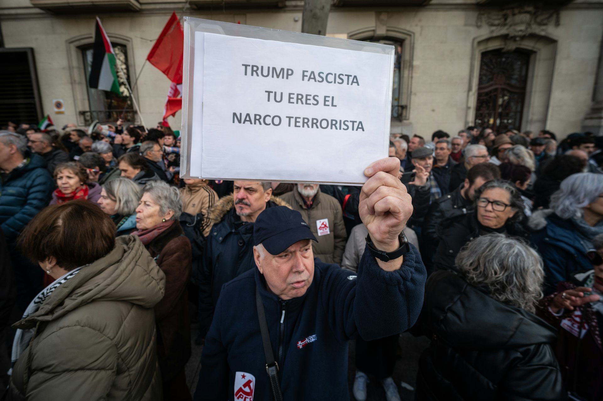 A Spanish protester holds a white sign with a message that Trump is a fascist and narco-terrorist.