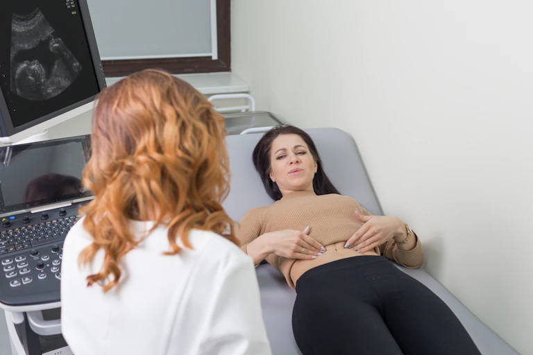 A woman lying on medical bed, about to have an abdominal scan, gestures to pain in her abdomen