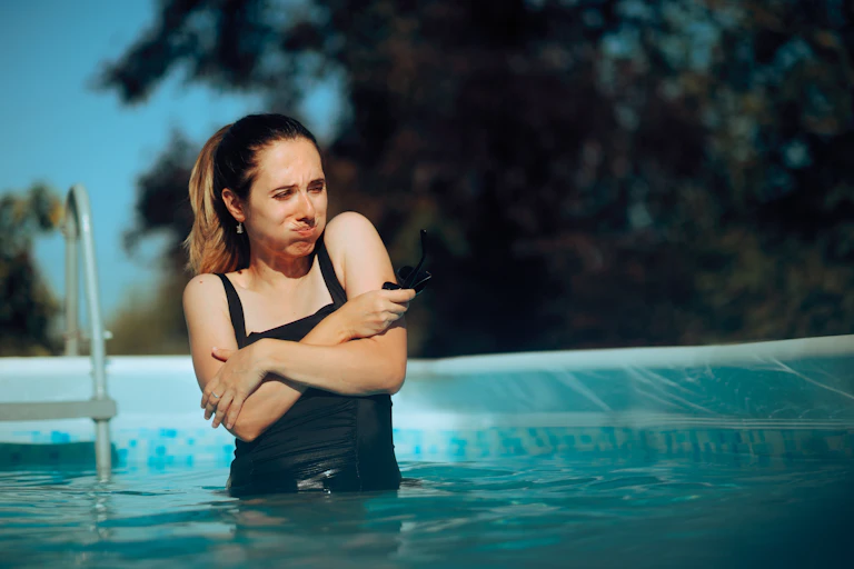 Woman shivering as she gets into pool.