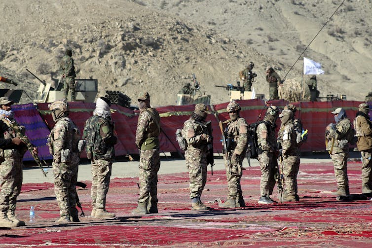 Several men dressed in military gear stand guard.