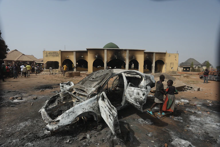 A burned out car is seen in front of a building.