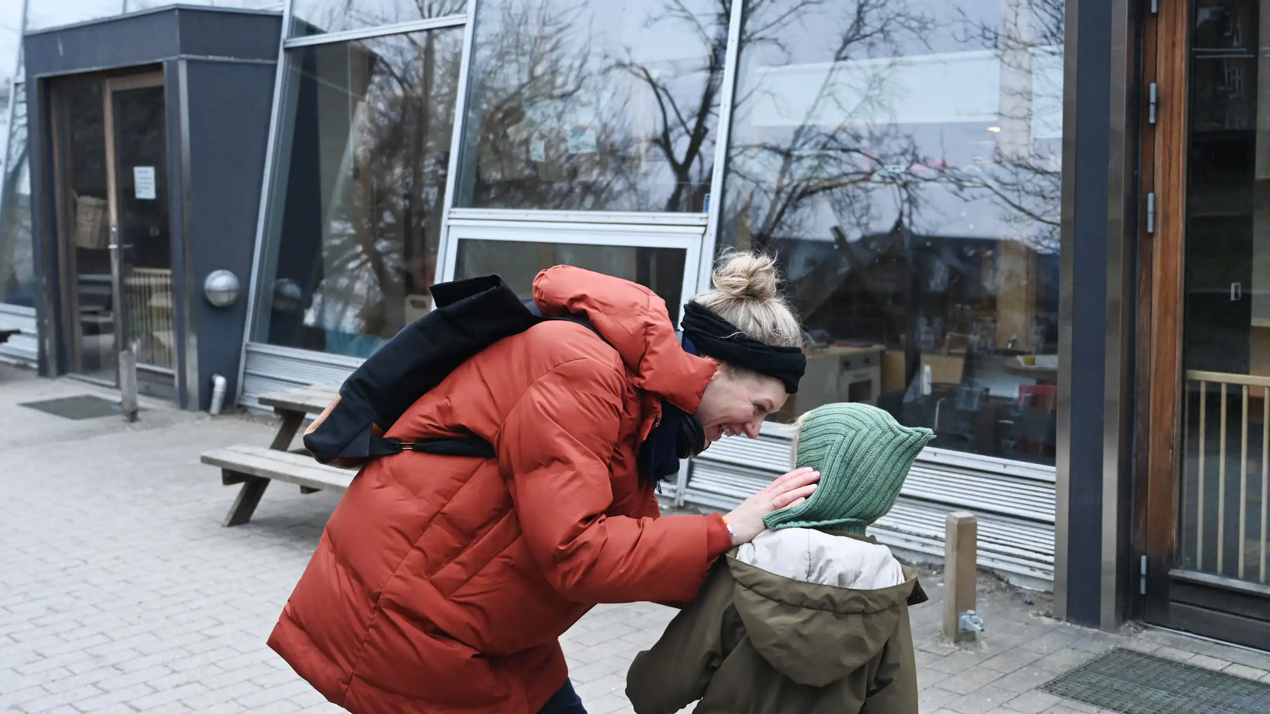 A woman in a parka leans over a child who is wearing a knit cap.