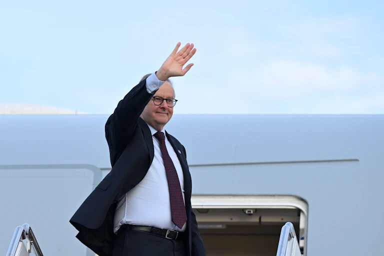 Anthony Albanese waves as he steps down from a plane.
