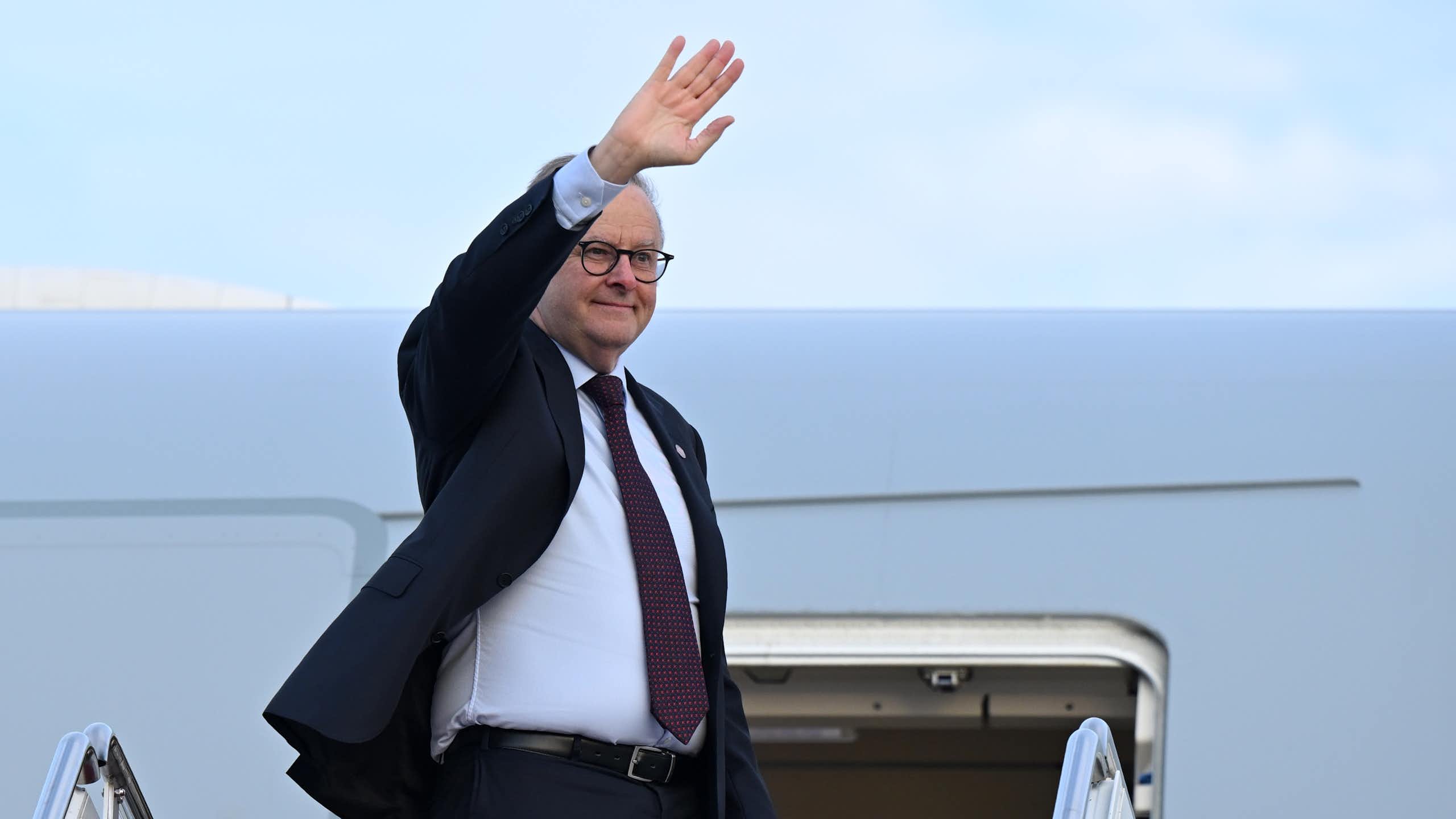 Anthony Albanese waves as he steps down from a plane.