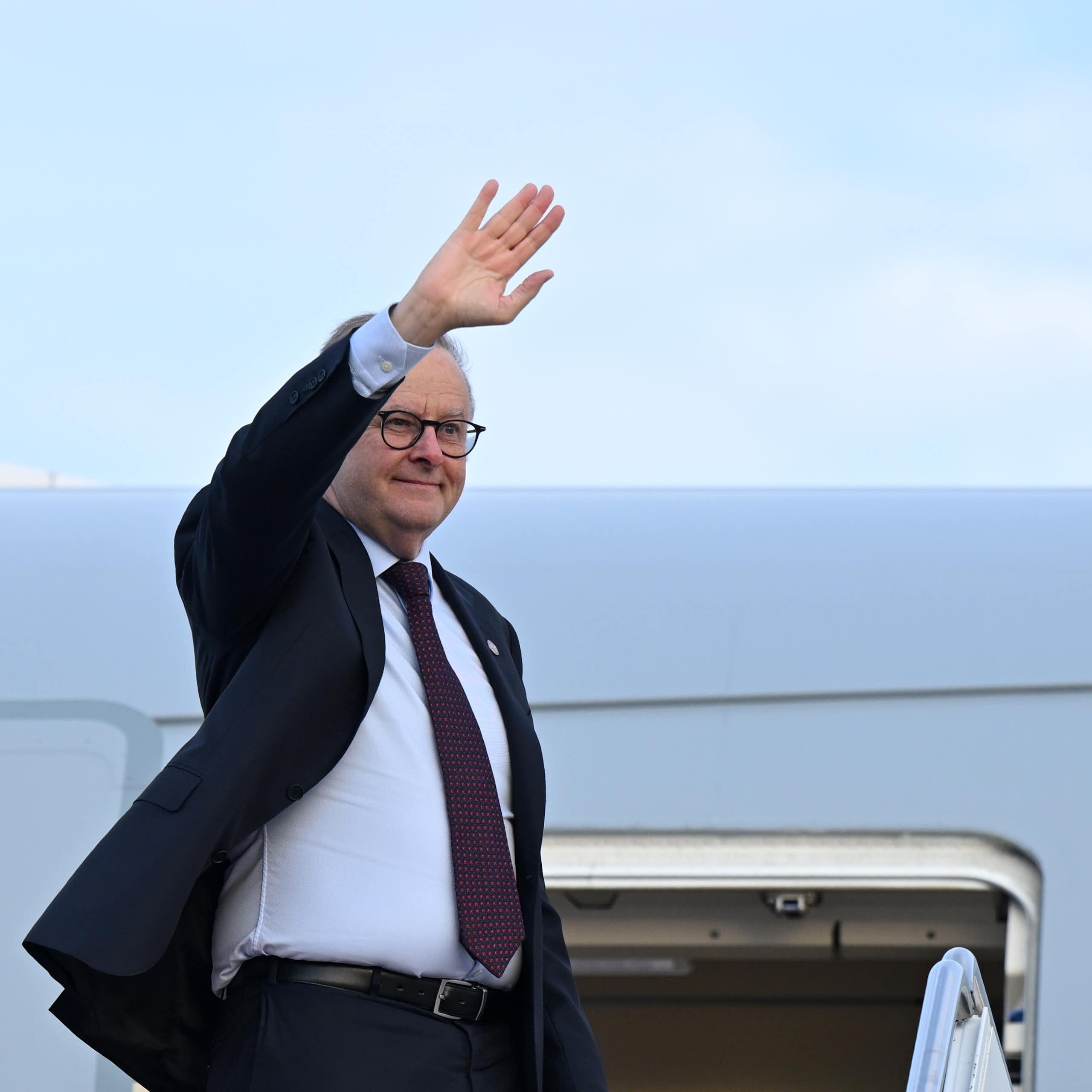 Anthony Albanese waves as he steps down from a plane.