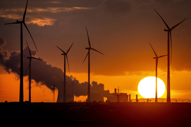 wind turbines silhouetted against coal plant.