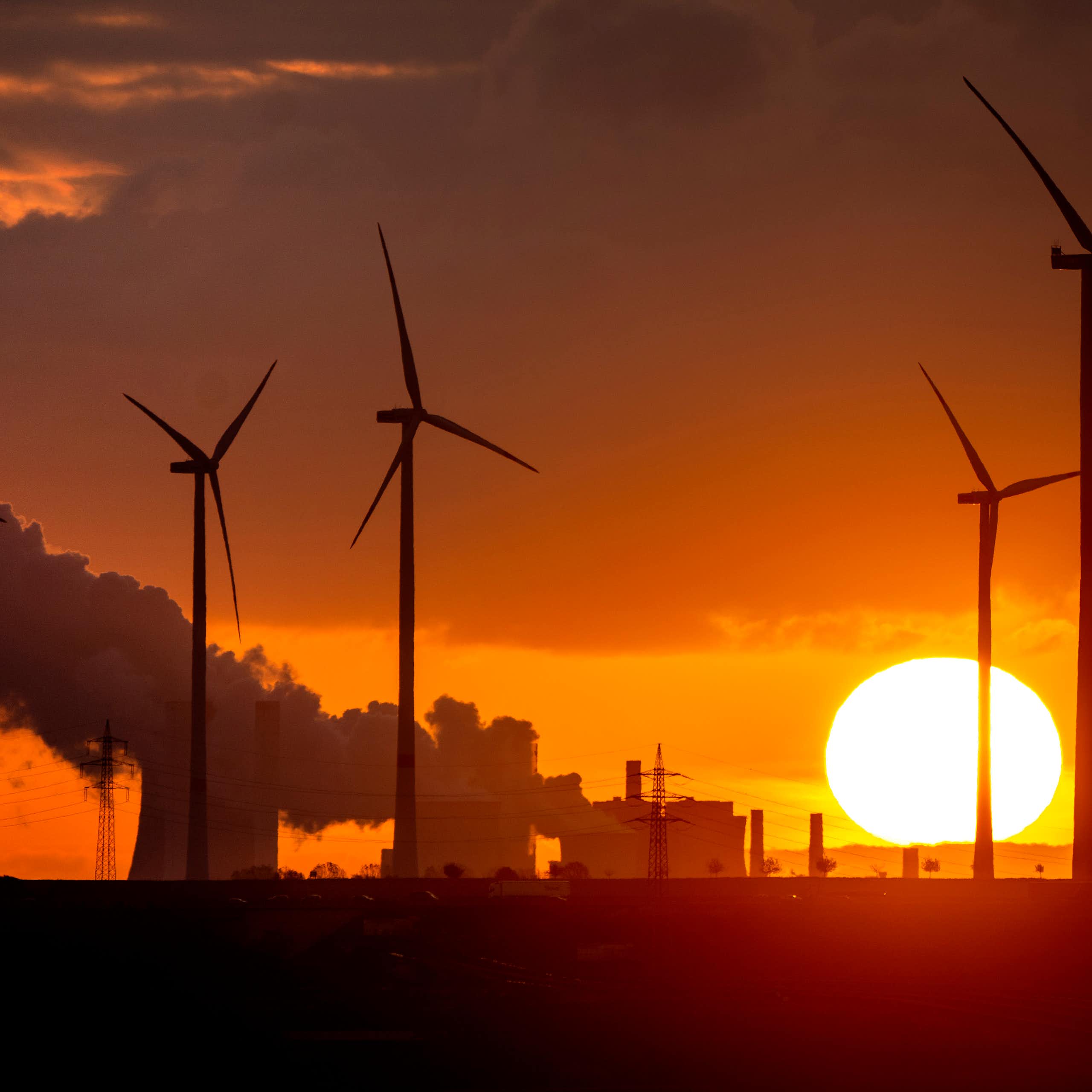wind turbines silhouetted against coal plant.