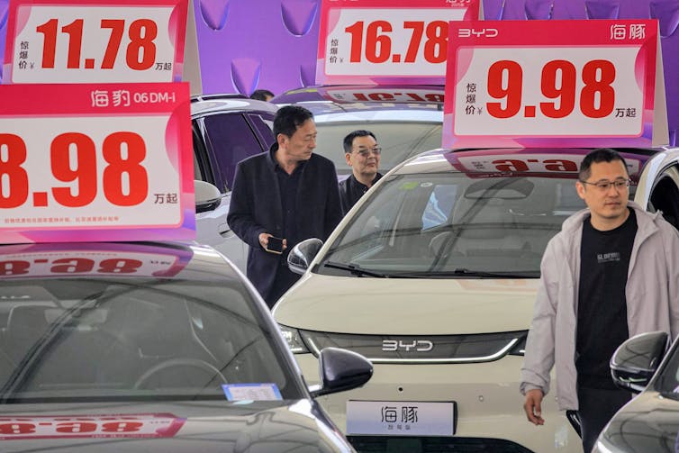 Shoppers in China check out cars with large prices on the top.