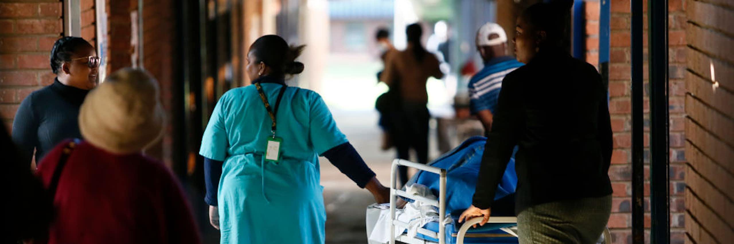 People pushing a mobile hospital bed in a corridor