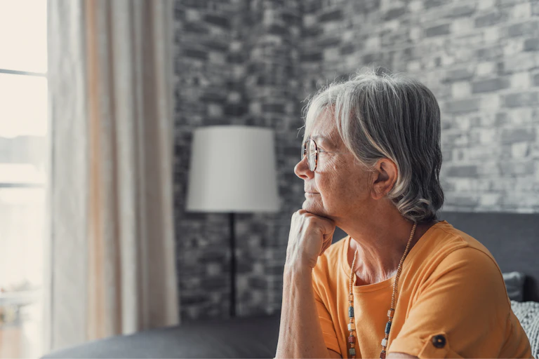 An older woman rests her head on her fist while looking out a window.