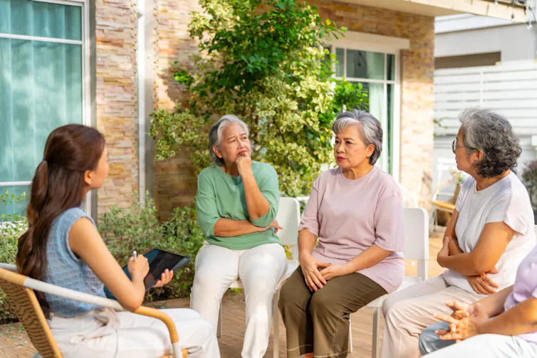 A group of three older women and one younger woman sit in a circle and talk outside.