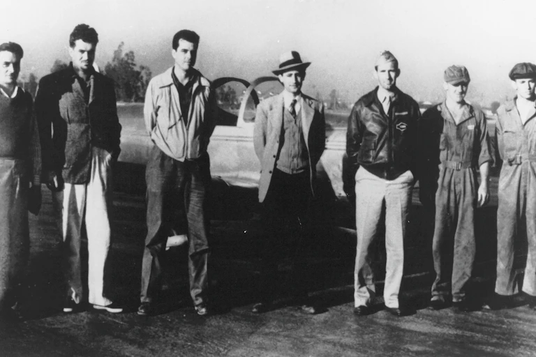 Rocket engineers lined up in front of an aircraft including Frank Malina (centre).