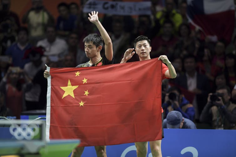 Dos jugadores chinos sostienen una bandera roja con estrellas amarillas en una esquina.
