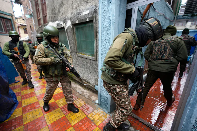 Heavily armed and masked security personnel enter a home.