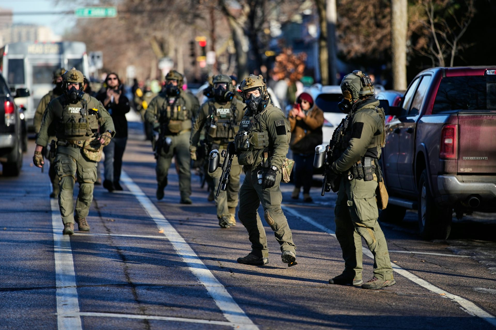 A group of uniformed ICE personnel walk along cars in a bike lane.