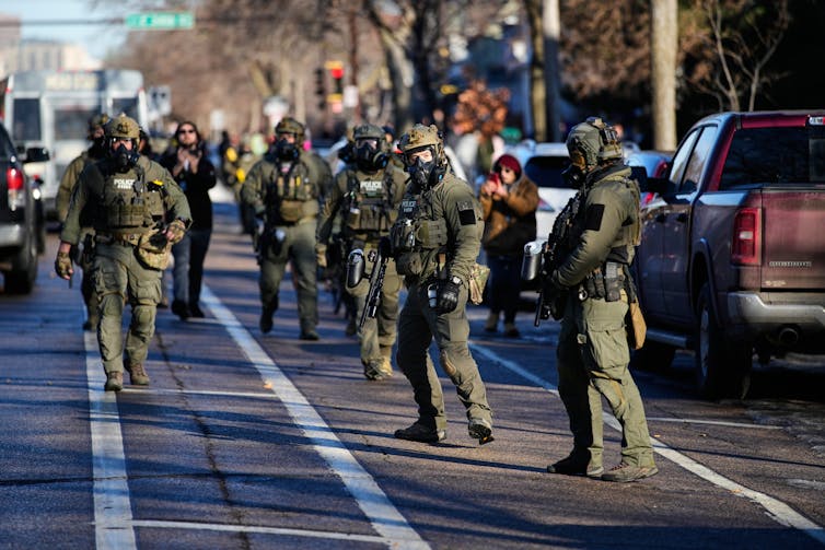 A group of uniformed ICE personnel walk along cars in a bike lane.