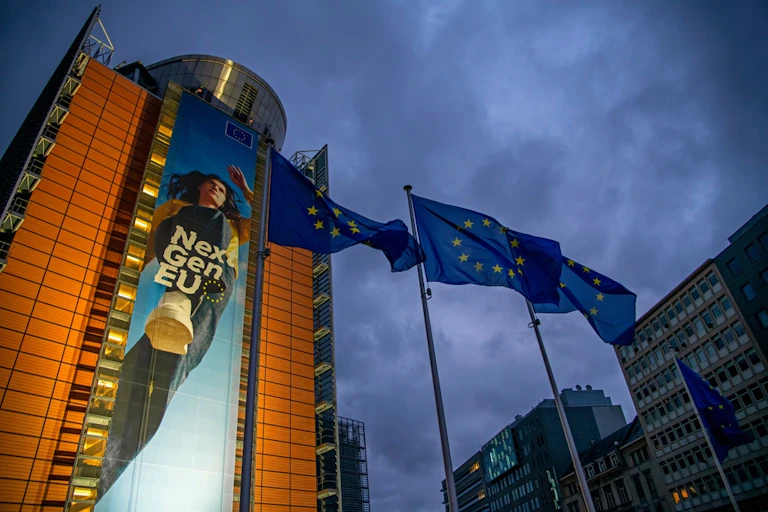 Cartel enorme que anuncia los fondos Next Generation en un edificio moderno al que preceden banderas de la UE.