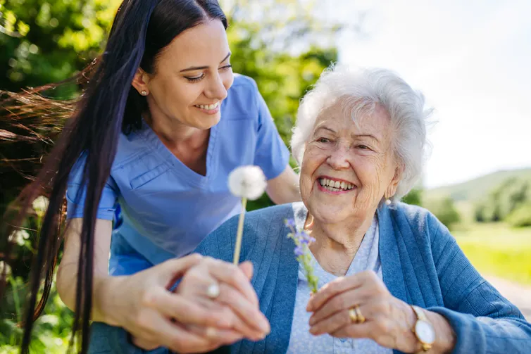An elderly lady and her carer, outside in a park.