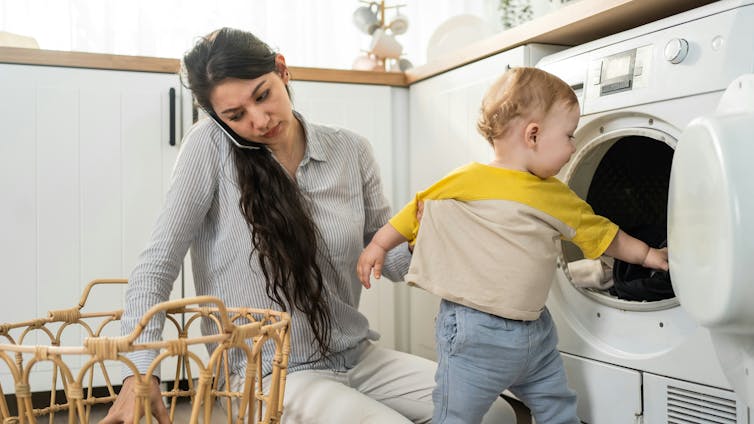 Una mujer que realiza múltiples tareas, lava la ropa y cuida a su hijo.