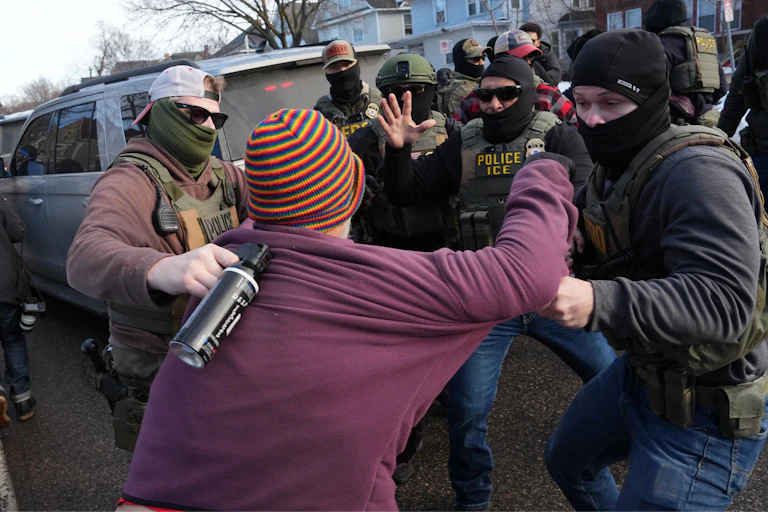 A woman is grabbed by federal agents who are in a cluster around her.