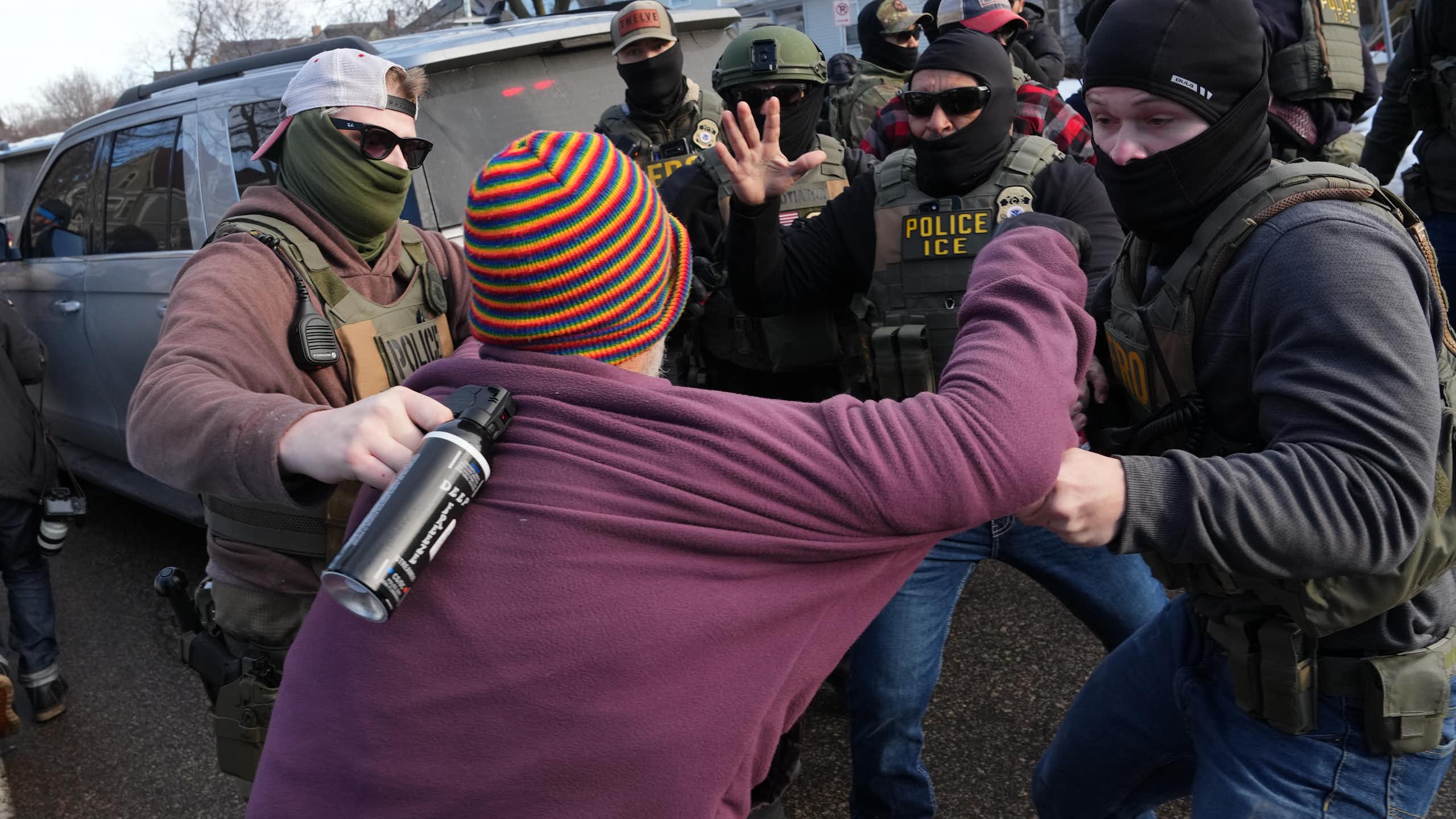 A woman is grabbed by federal agents who are in a cluster around her.