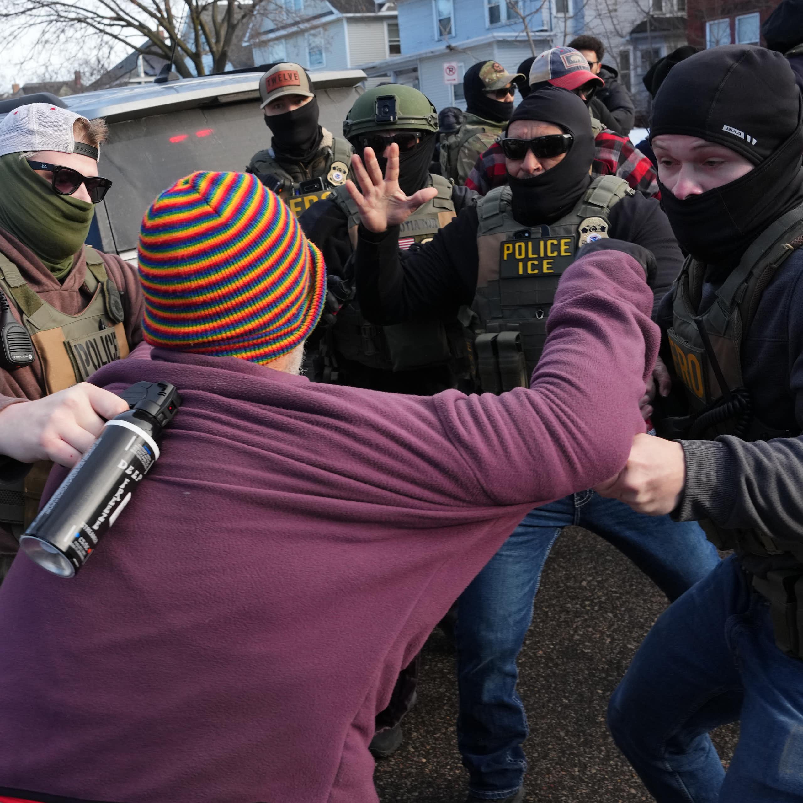 A woman is grabbed by federal agents who are in a cluster around her.