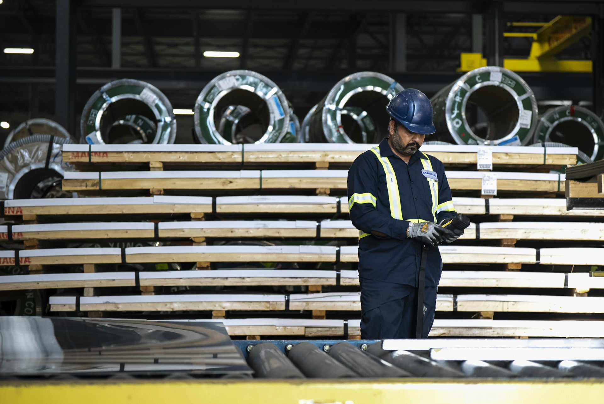 A worker in a hard hat looks at coils of stainless steel on a conveyer belt