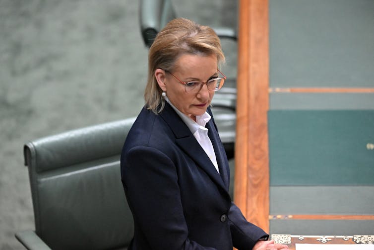 A woman stands at a green table and looks seriously to her right