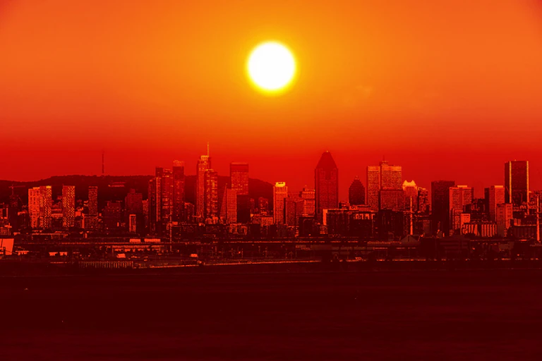 A red sun rises over a city, in an atmosphere of heat.