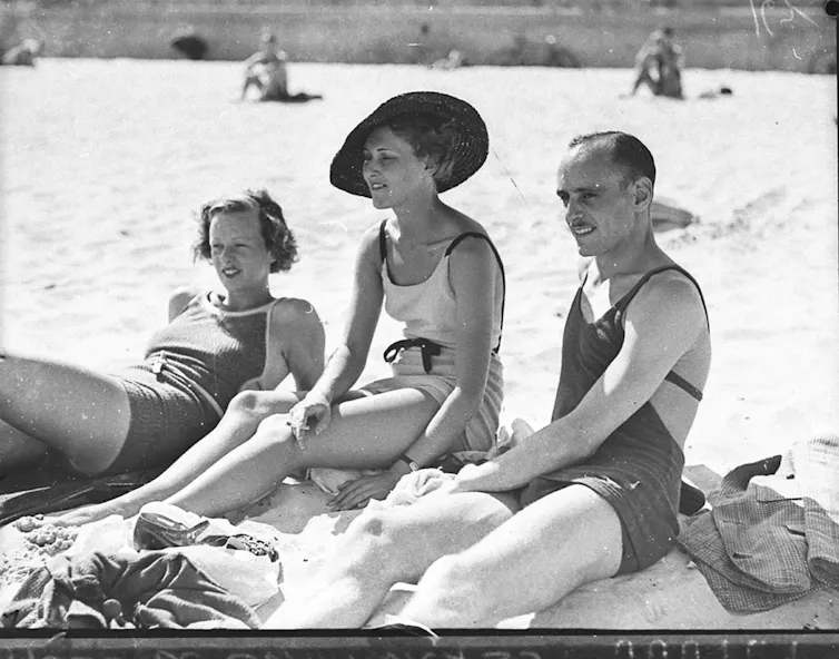 Three people in bathers, one woman wears a hat