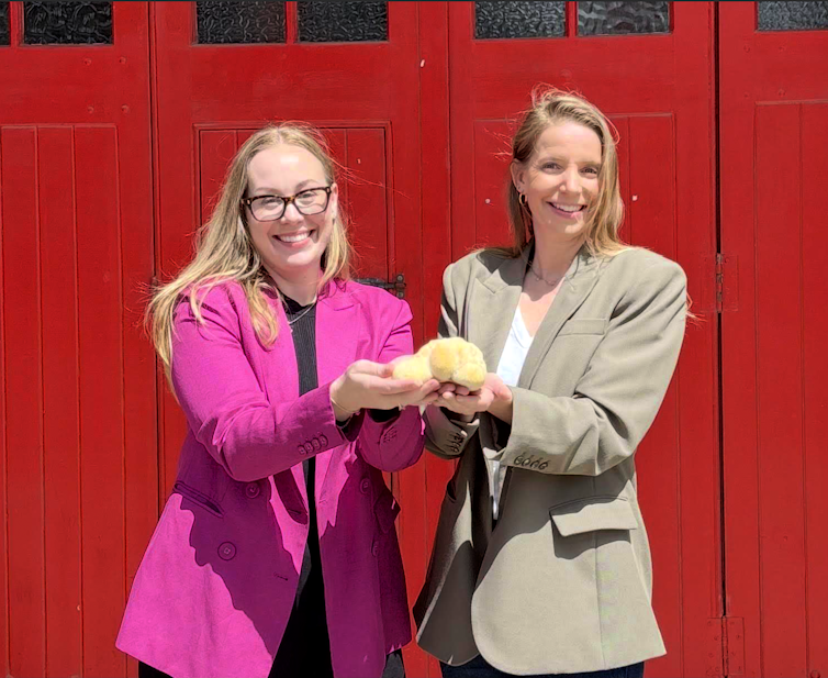 Two women standing in front of a red door, holding white mushrooms.